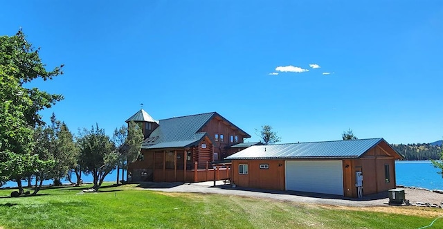 view of front of property featuring a detached garage, a front lawn, a water view, metal roof, and an outbuilding