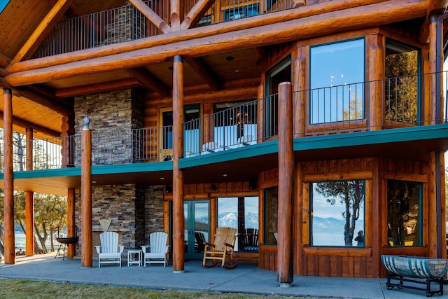 back of property featuring stone siding, a balcony, a patio, and log exterior