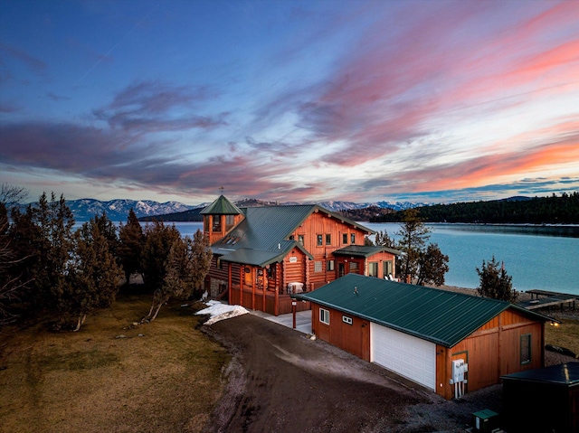 view of front facade with a front lawn, driveway, an outdoor structure, metal roof, and a water and mountain view