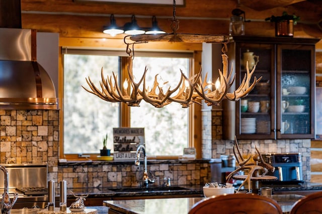 kitchen with glass insert cabinets, plenty of natural light, wall chimney exhaust hood, and a sink