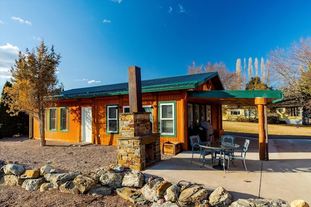 back of property with board and batten siding, a patio, a chimney, and metal roof