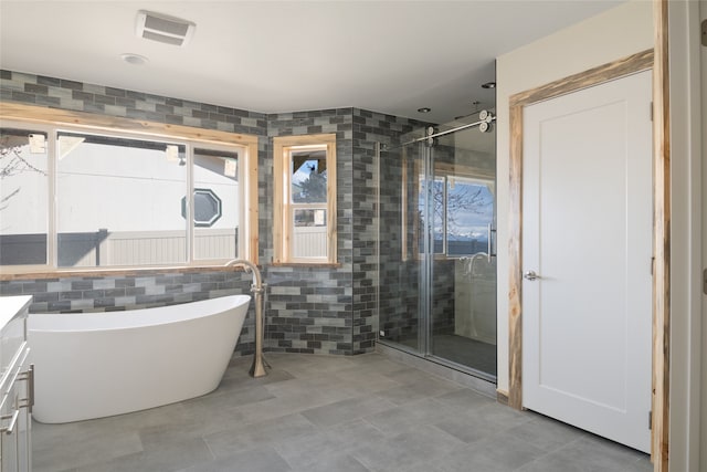 bathroom with vanity, visible vents, a soaking tub, a stall shower, and tile walls