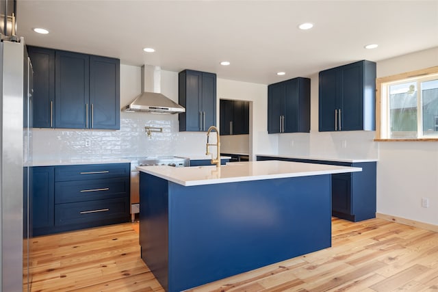 kitchen featuring blue cabinetry, stainless steel appliances, a sink, and wall chimney range hood