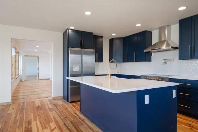 kitchen featuring light wood finished floors, blue cabinetry, freestanding refrigerator, light countertops, and wall chimney exhaust hood