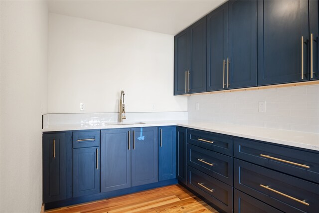 kitchen featuring light countertops, blue cabinets, light wood finished floors, and a sink