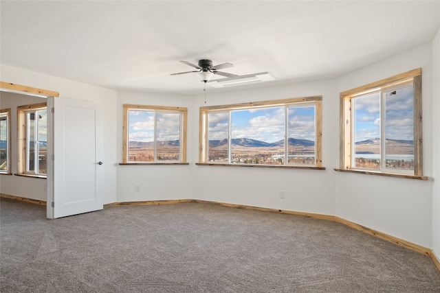 carpeted empty room with a mountain view, a ceiling fan, and baseboards