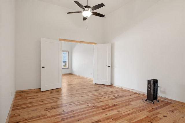 unfurnished room featuring light wood-style flooring, a ceiling fan, a high ceiling, and baseboards