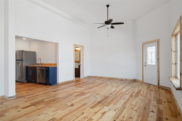 unfurnished living room featuring a sink, baseboards, a high ceiling, and light wood finished floors