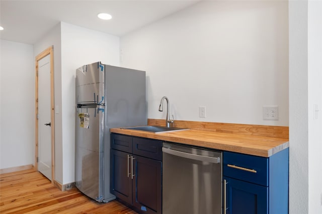 kitchen with light wood-style flooring, blue cabinetry, a sink, stainless steel appliances, and butcher block counters