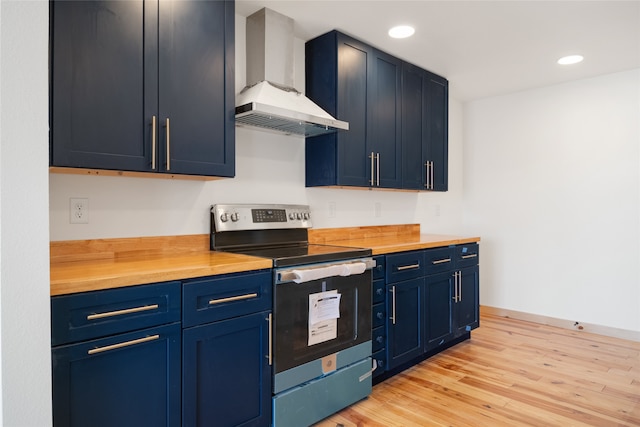 kitchen featuring stainless steel electric range oven, wooden counters, light wood finished floors, blue cabinetry, and wall chimney exhaust hood