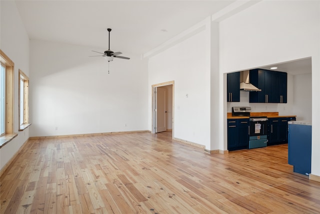 unfurnished living room with light wood-style flooring, baseboards, a towering ceiling, and a ceiling fan