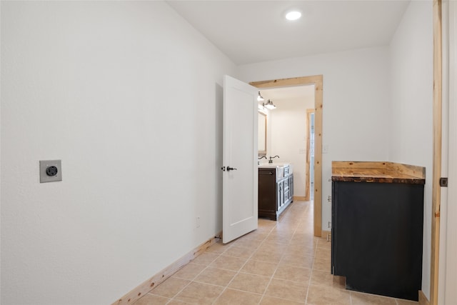 corridor featuring light tile patterned floors, baseboards, and a sink