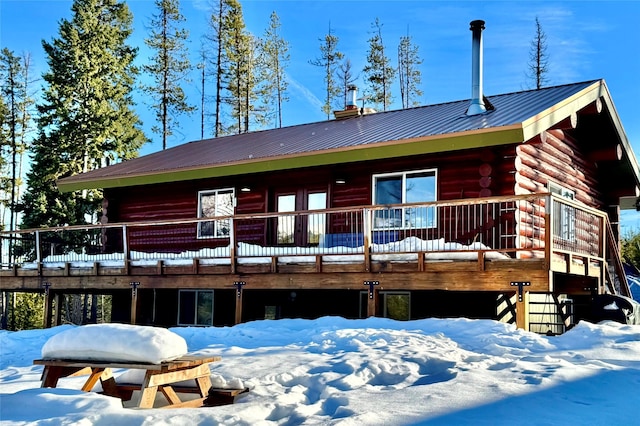 snow covered back of property with log exterior and metal roof