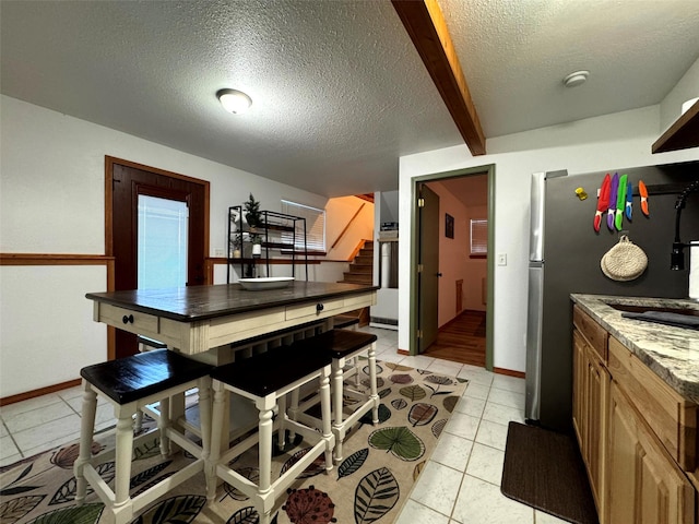 kitchen featuring baseboards, beamed ceiling, light tile patterned flooring, a textured ceiling, and a sink