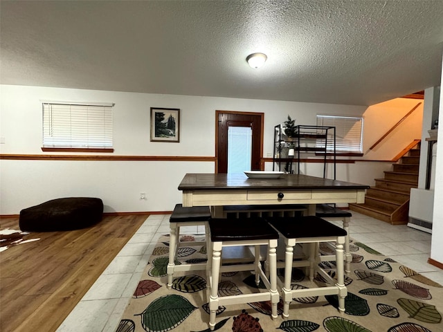 dining room with light tile patterned floors, stairway, a textured ceiling, and baseboards