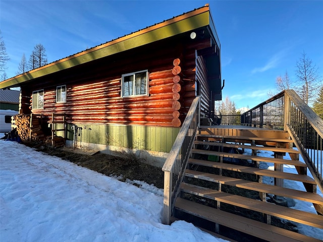 snow covered property with stairs, log siding, and metal roof