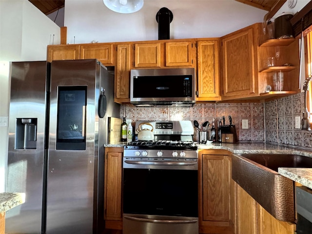 kitchen featuring brown cabinets, tasteful backsplash, appliances with stainless steel finishes, lofted ceiling, and light stone countertops