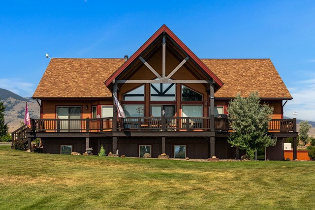 rear view of property featuring a deck with mountain view, a lawn, and roof with shingles