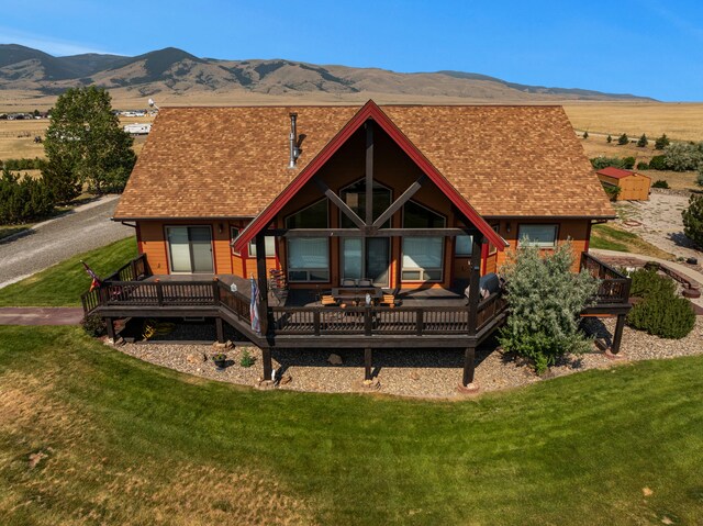 back of house featuring a yard, a deck with mountain view, and roof with shingles