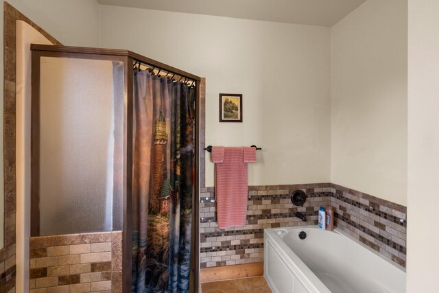 bathroom with tile patterned flooring, a shower stall, wainscoting, a bath, and tile walls