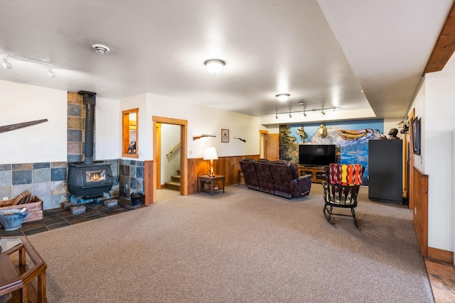 living room featuring carpet, stairs, wainscoting, rail lighting, and a wood stove