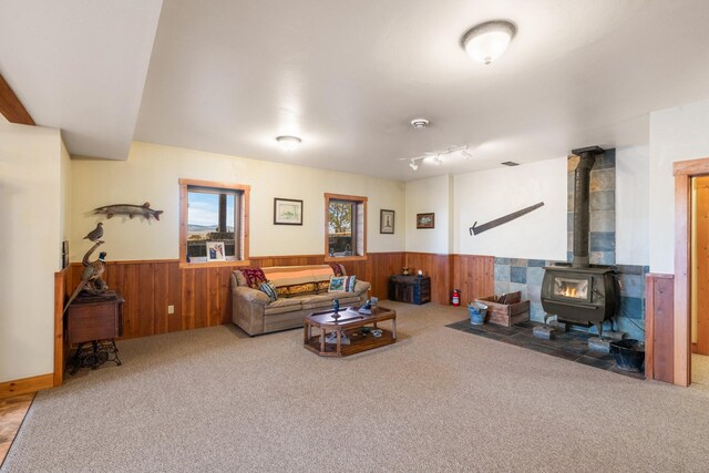 carpeted living room with a wood stove, wood walls, and wainscoting