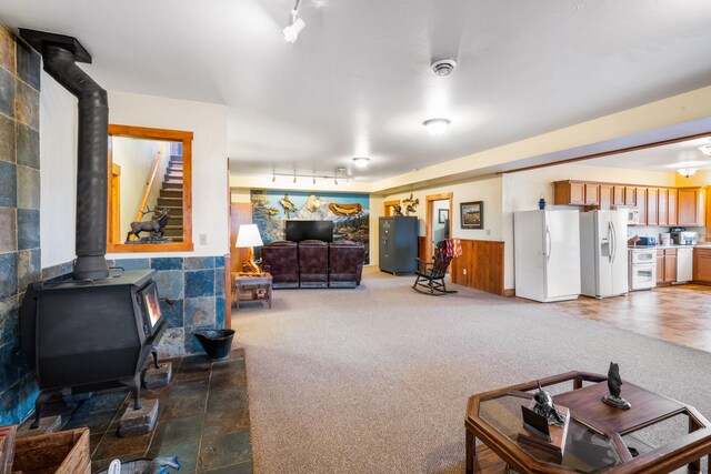 carpeted living area with a wood stove and wainscoting