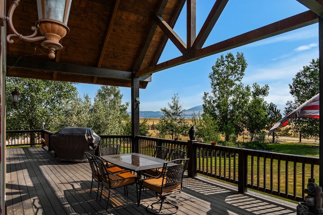 deck with area for grilling, outdoor dining area, a mountain view, and a yard