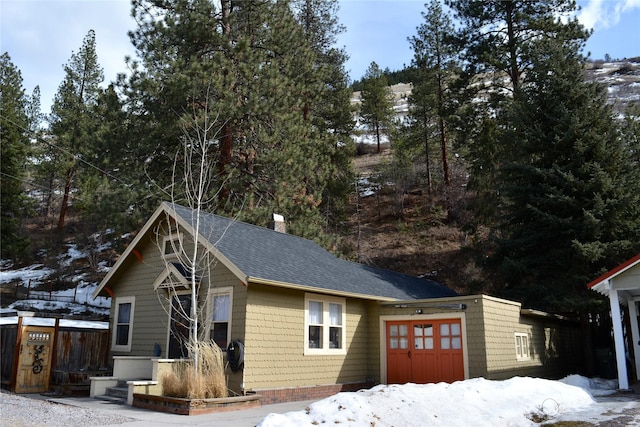 view of front facade featuring a chimney, a shingled roof, a garage, and fence