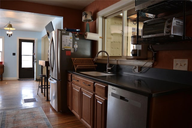 kitchen featuring wood finished floors, visible vents, a sink, stainless steel appliances, and dark countertops