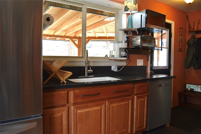 kitchen with dark countertops, brown cabinets, appliances with stainless steel finishes, and a sink