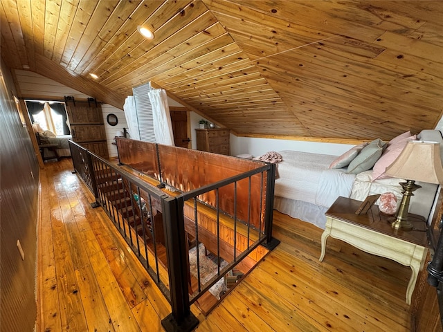 hallway with wood walls, lofted ceiling, hardwood / wood-style floors, an upstairs landing, and wooden ceiling