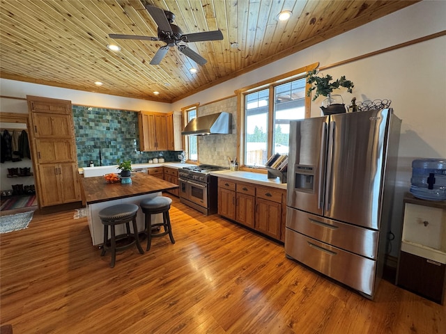 kitchen featuring stainless steel appliances, wood ceiling, wall chimney range hood, brown cabinets, and backsplash