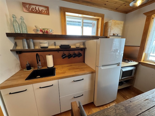 kitchen featuring open shelves, a sink, butcher block counters, and freestanding refrigerator