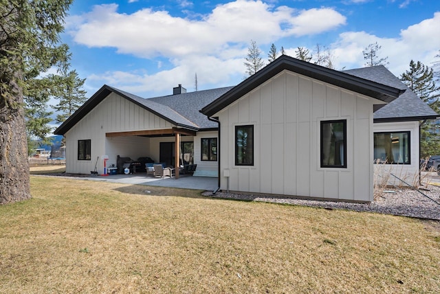 rear view of house featuring board and batten siding, roof with shingles, a lawn, a chimney, and a patio area