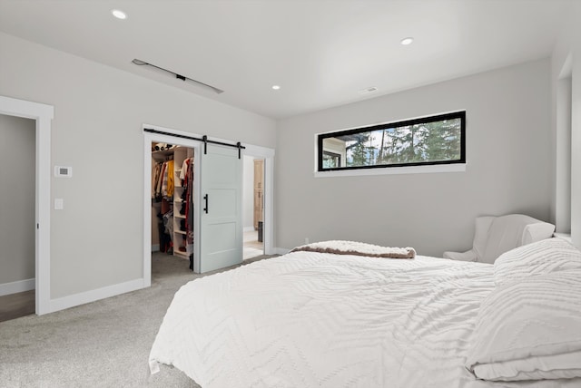 bedroom with baseboards, recessed lighting, a spacious closet, light carpet, and a barn door