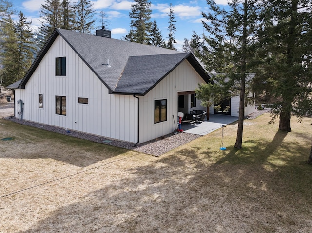 view of side of property with board and batten siding, roof with shingles, a chimney, a yard, and a patio area