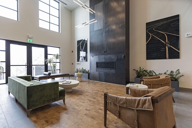 living room featuring french doors, a large fireplace, baseboards, and a towering ceiling