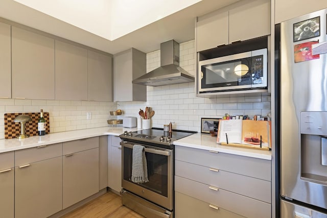 kitchen featuring tasteful backsplash, appliances with stainless steel finishes, wall chimney exhaust hood, and gray cabinetry