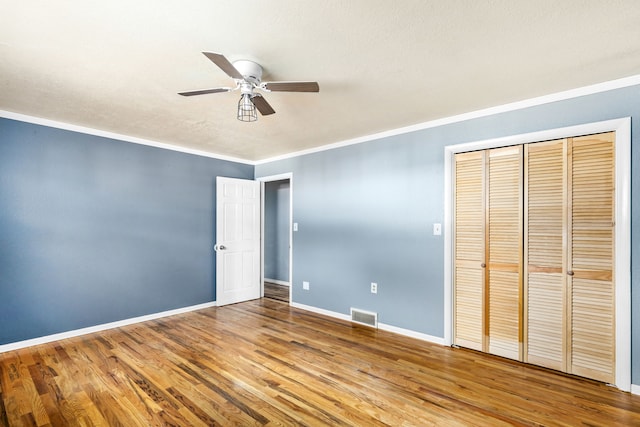 unfurnished bedroom featuring visible vents, ornamental molding, wood finished floors, a closet, and baseboards