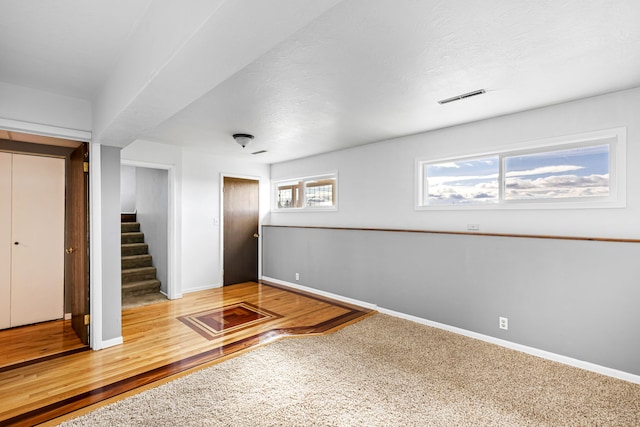 empty room featuring wood finished floors, baseboards, visible vents, stairs, and a textured ceiling