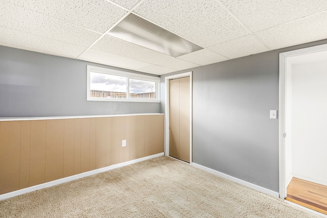 unfurnished bedroom featuring baseboards, carpet, a drop ceiling, a wainscoted wall, and a closet