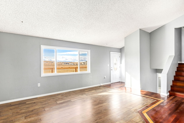 unfurnished living room featuring stairway, baseboards, a textured ceiling, and hardwood / wood-style floors