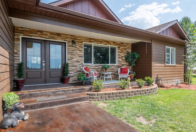 entrance to property featuring a lawn, stone siding, french doors, covered porch, and board and batten siding