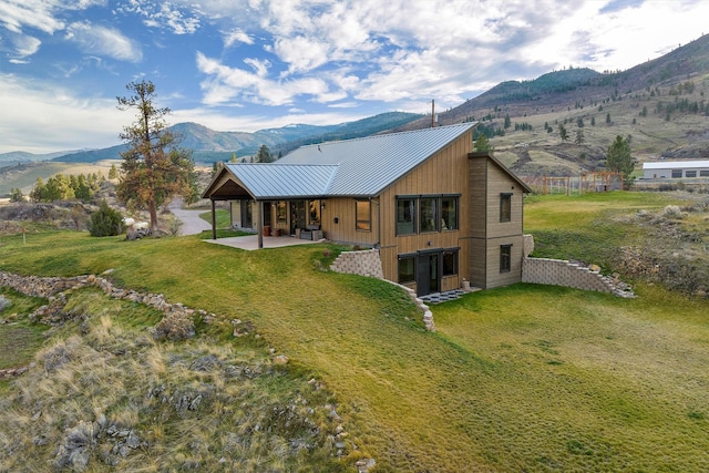 back of property featuring a mountain view, a lawn, metal roof, and a patio area