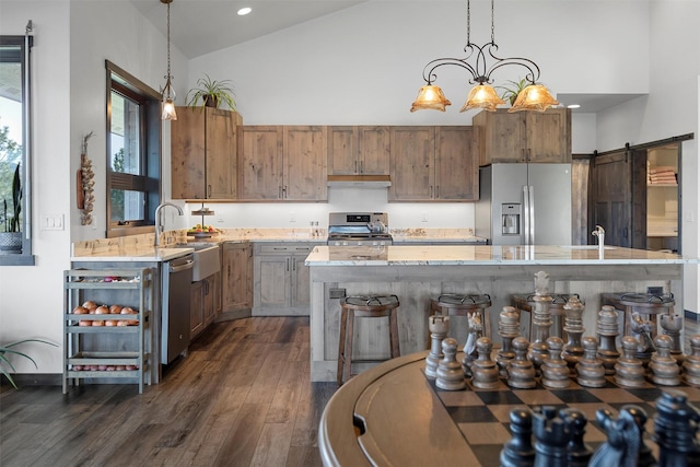 kitchen featuring light stone counters, high vaulted ceiling, a sink, appliances with stainless steel finishes, and a barn door