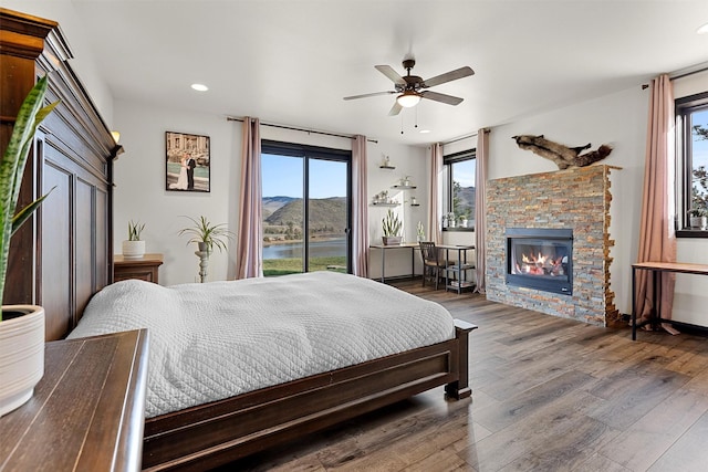 bedroom featuring a stone fireplace, recessed lighting, wood finished floors, a water and mountain view, and access to outside