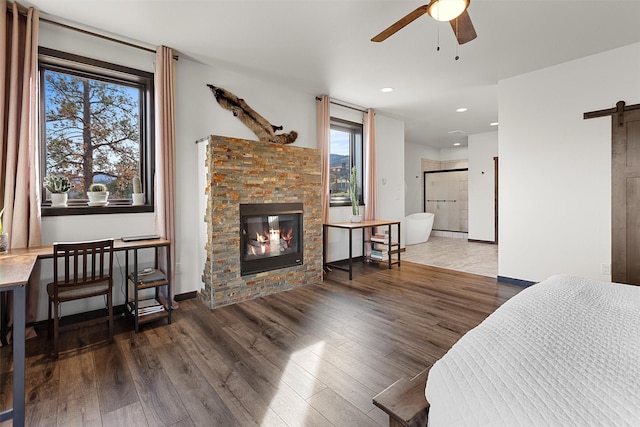 living area with ceiling fan, baseboards, a barn door, a stone fireplace, and wood finished floors