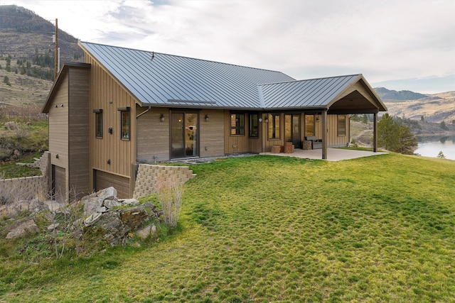 back of house featuring a standing seam roof, a lawn, metal roof, a patio area, and a water and mountain view