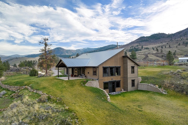 rear view of property featuring a patio, a lawn, a mountain view, and metal roof